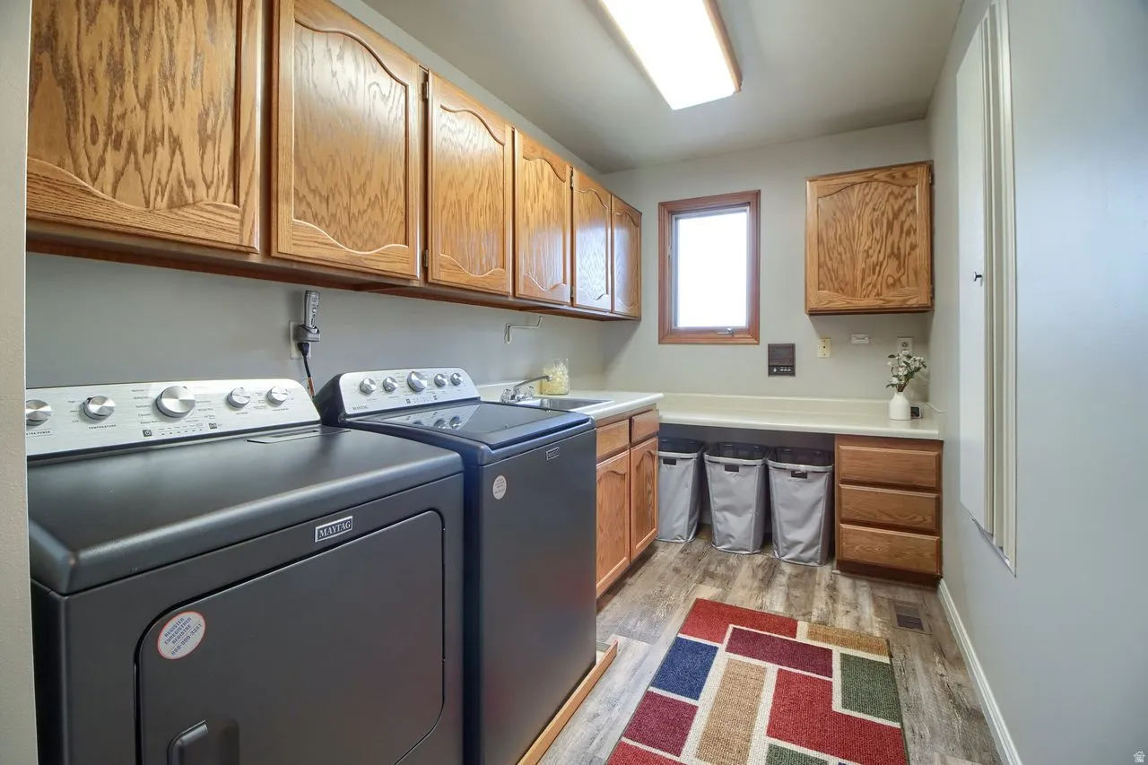 Laundry room with independent washer and dryer, cabinet space, and light wood-style flooring