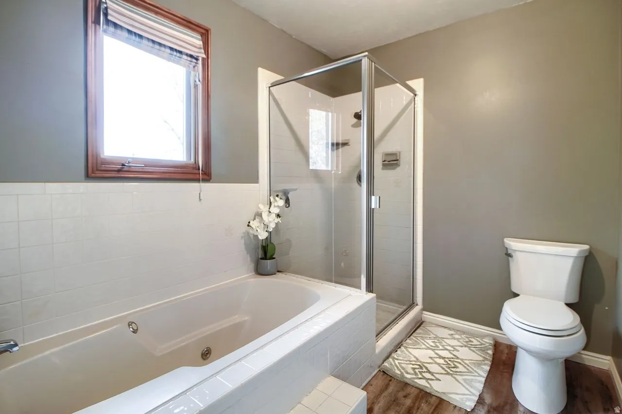 Full bath featuring a shower stall, a jetted tub, and wood finished floors