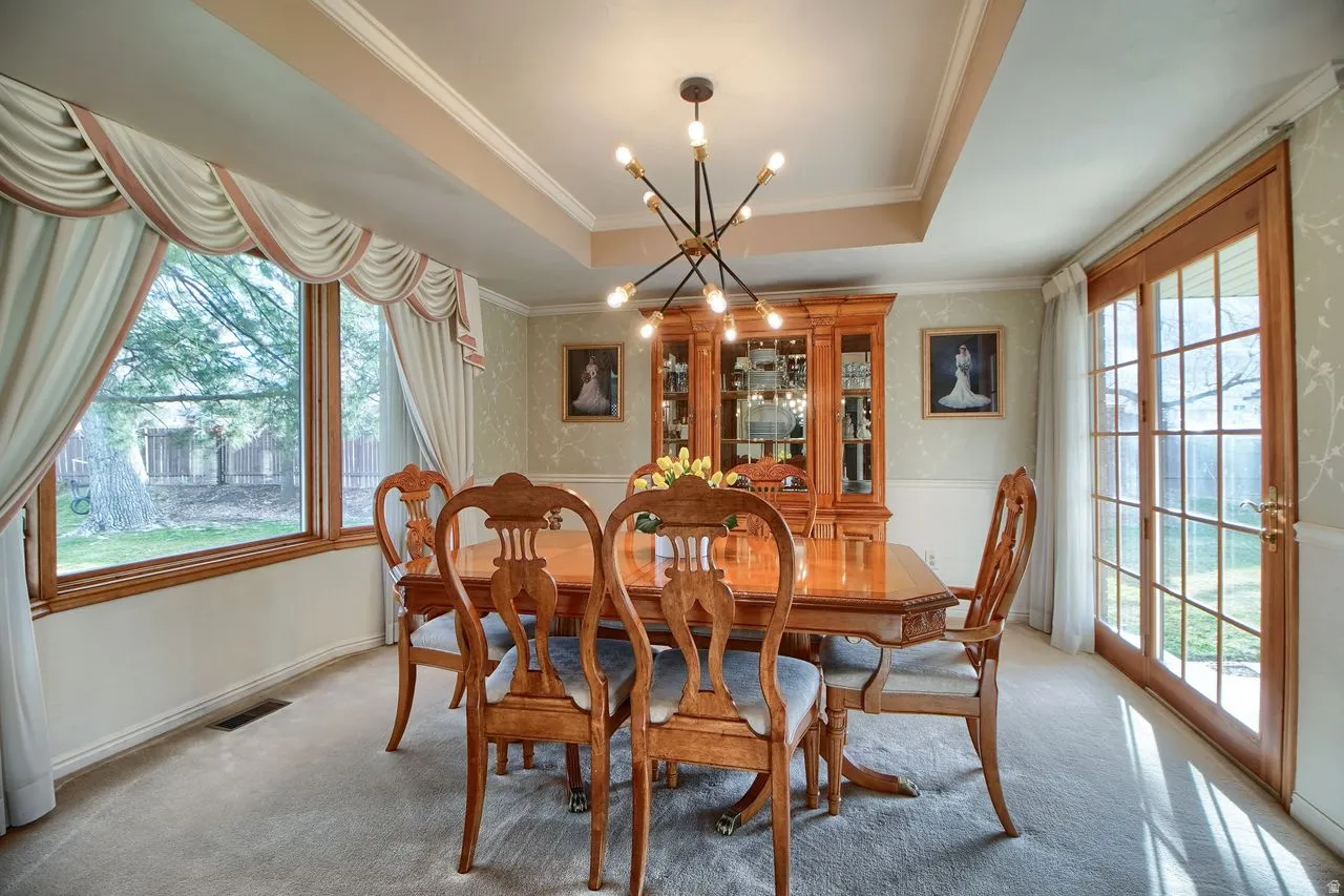 Dining space with a raised ceiling, plenty of natural light, suspended lighting, light carpet, and ornamental molding