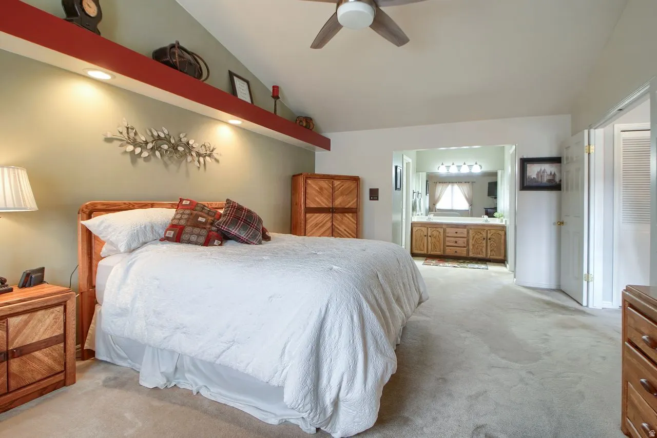 Bedroom featuring carpet floors, lofted ceiling, a ceiling fan, and ensuite bathroom