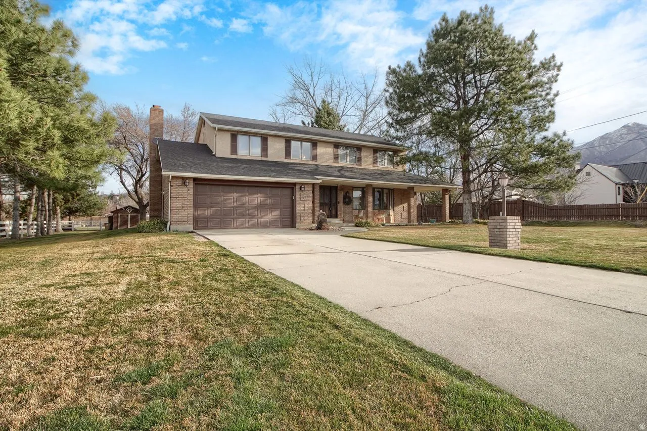 View of front of home featuring a chimney, driveway, brick siding, and a porch