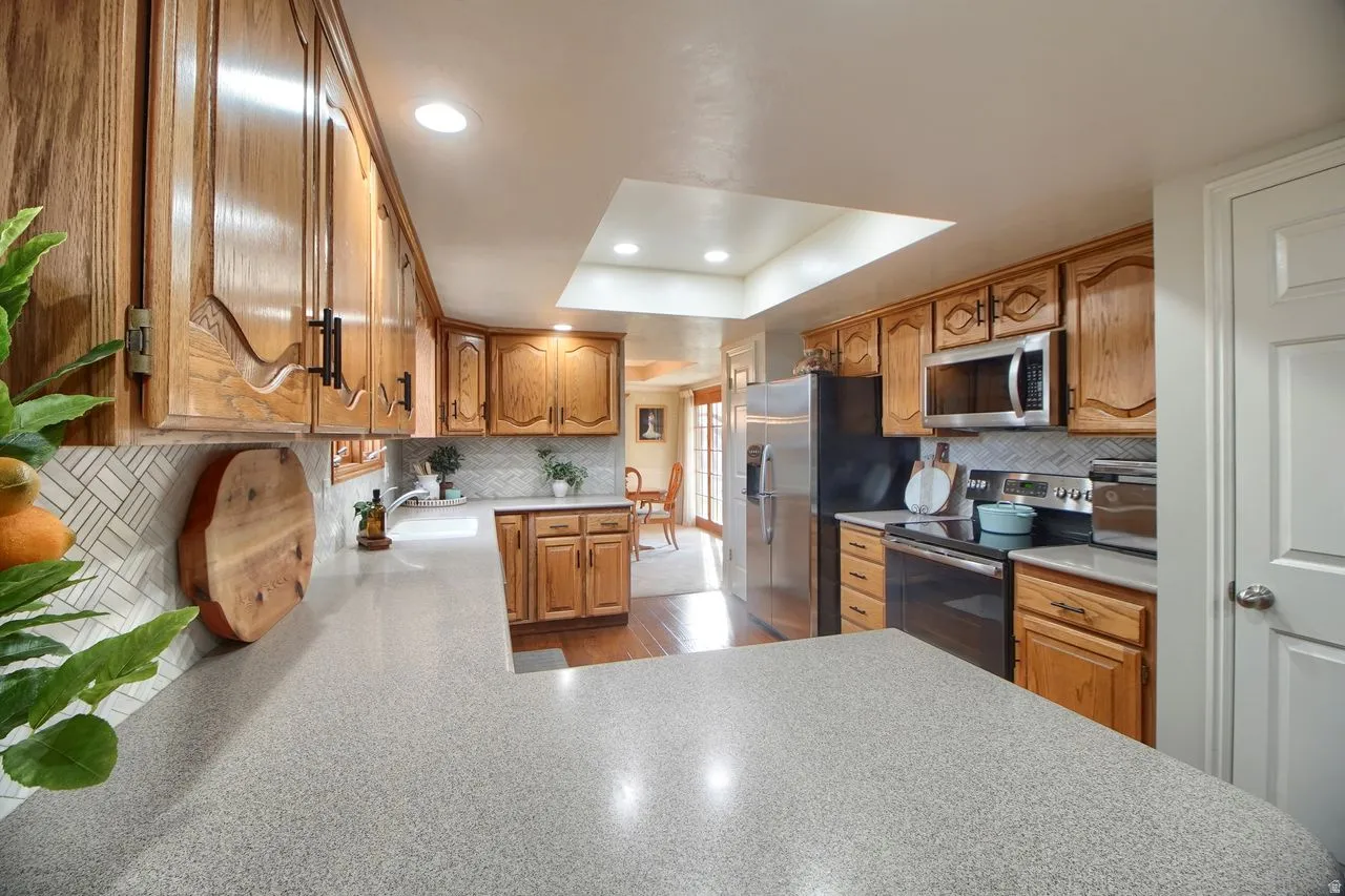 Kitchen featuring stainless steel appliances, wood finish cabinets, recessed lighting, a raised ceiling, and light countertops