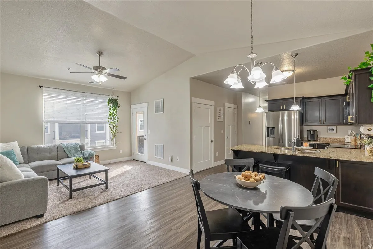 Dining space featuring a chandelier, light wood-style floors, a ceiling fan, and vaulted ceiling