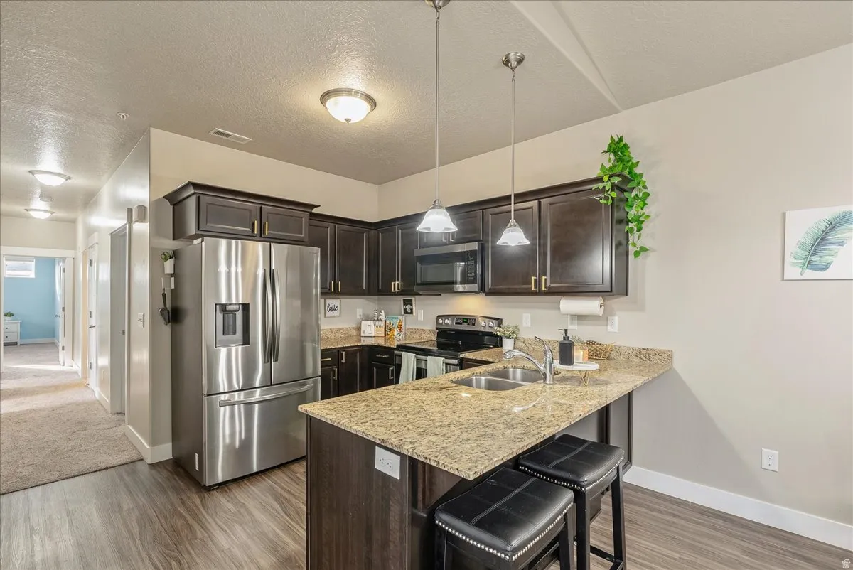 Kitchen with stainless steel appliances, dark wood finish cabinetry, a breakfast bar area, light stone countertops, and a peninsula