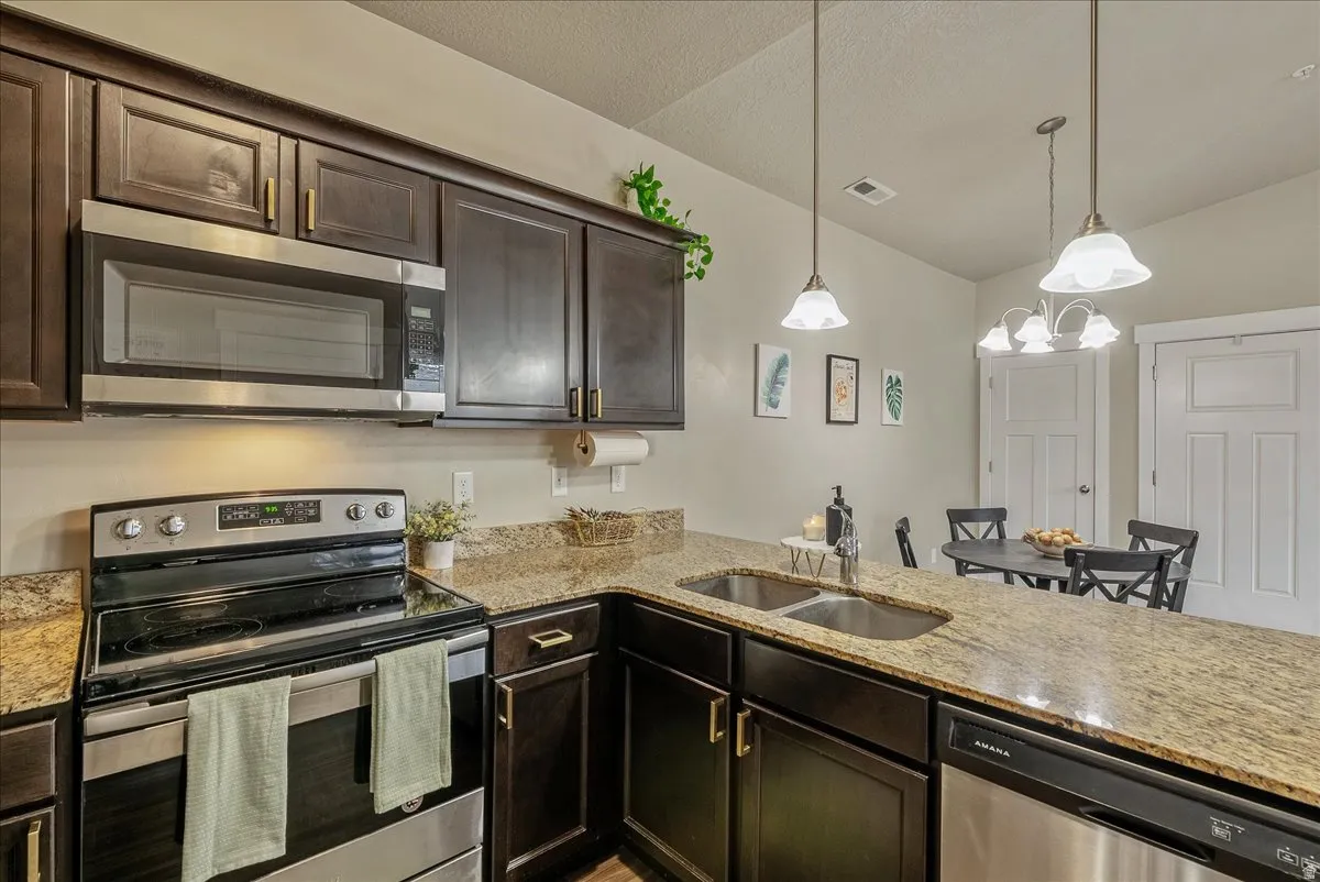 Kitchen featuring stainless steel appliances, dark wood finish cabinets, light stone countertops, a peninsula, and suspended lighting