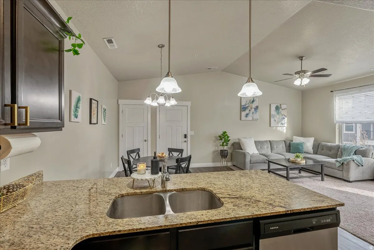 Kitchen with open floor plan, light stone countertops, dishwasher, pendant lighting, and a textured ceiling