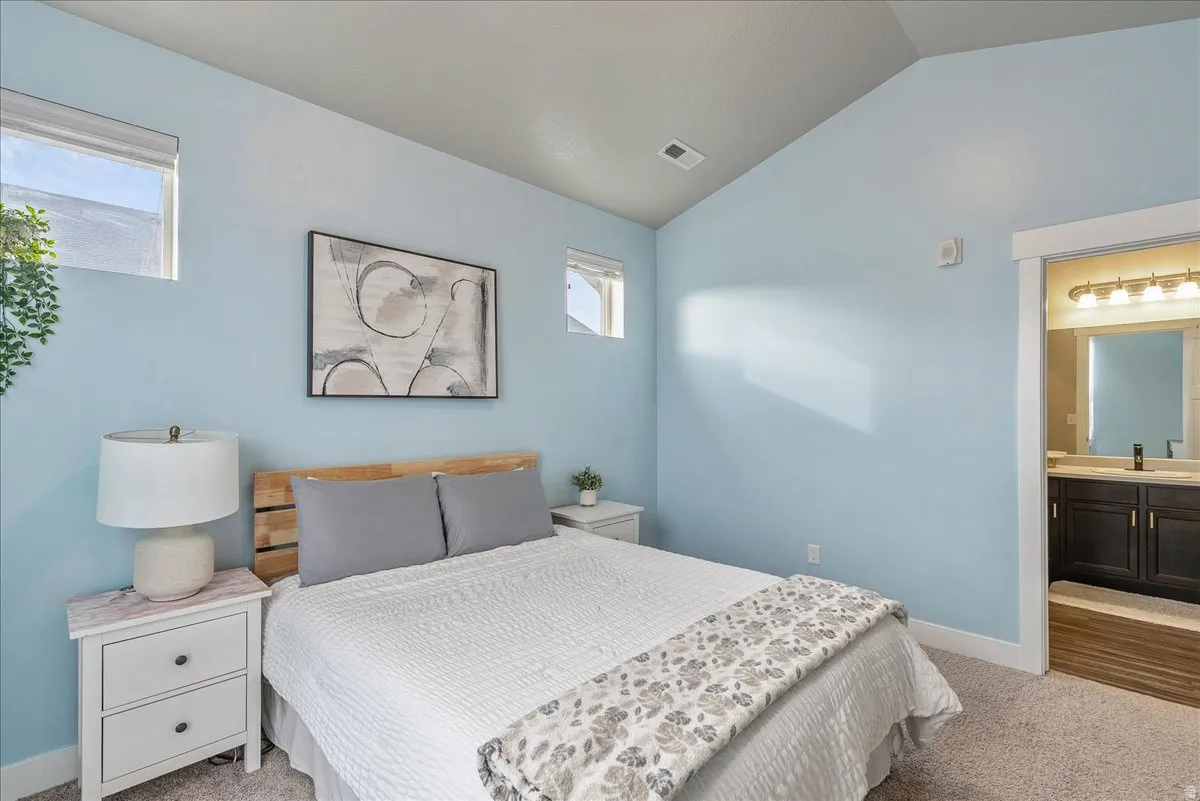 Bedroom featuring light carpet, lofted ceiling, and ensuite bath