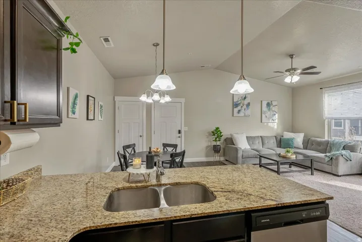 Kitchen with open floor plan, light stone countertops, dishwasher, pendant lighting, and a textured ceiling