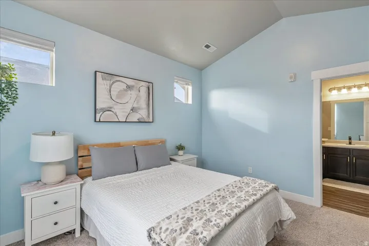 Bedroom featuring light carpet, lofted ceiling, and ensuite bath
