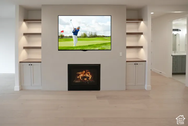 Unfurnished living room with built in shelves, light wood-style floors, and a lit fireplace