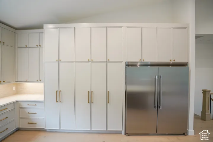 Kitchen with built in refrigerator, tasteful backsplash, light wood-type flooring, and light stone counters