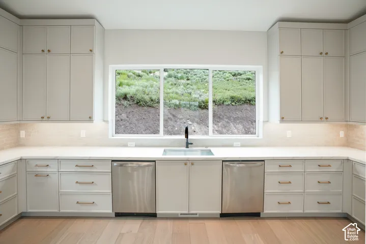 Kitchen with dishwasher, tasteful backsplash, light wood finished floors, and light stone countertops