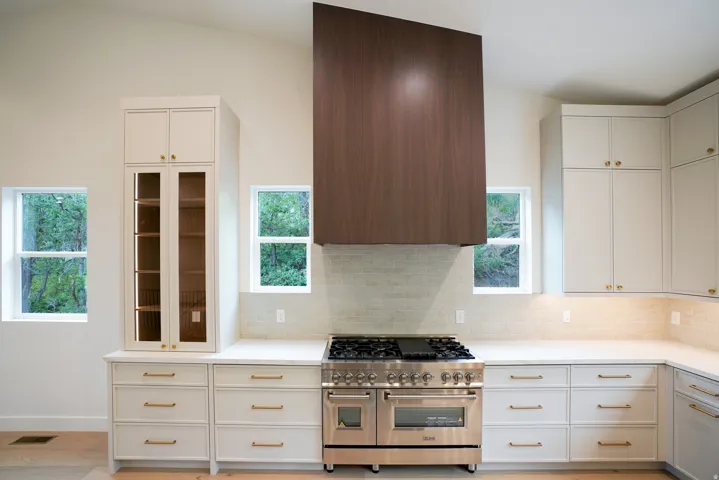 Kitchen with range with two ovens, white cabinetry, backsplash, and range hood