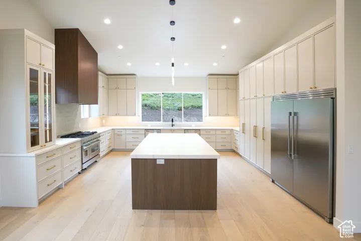 Kitchen featuring two tone cabinets, a center island, high end appliances, light stone countertops, and pendant lighting
