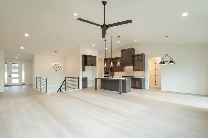 Unfurnished living room with suspended lighting, light wood-style flooring, and lofted ceiling