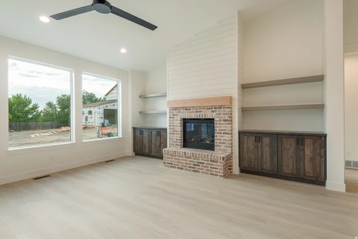 Unfurnished living room with lofted ceiling, light wood-style floors, ceiling fan, a brick fireplace, and recessed lighting