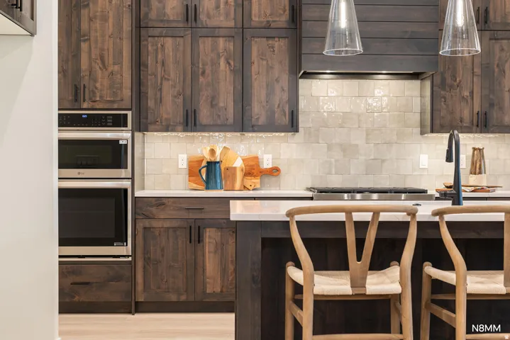 Kitchen with dark wood finish cabinets, stainless steel double oven, tasteful backsplash, a kitchen breakfast bar, and hanging light fixtures