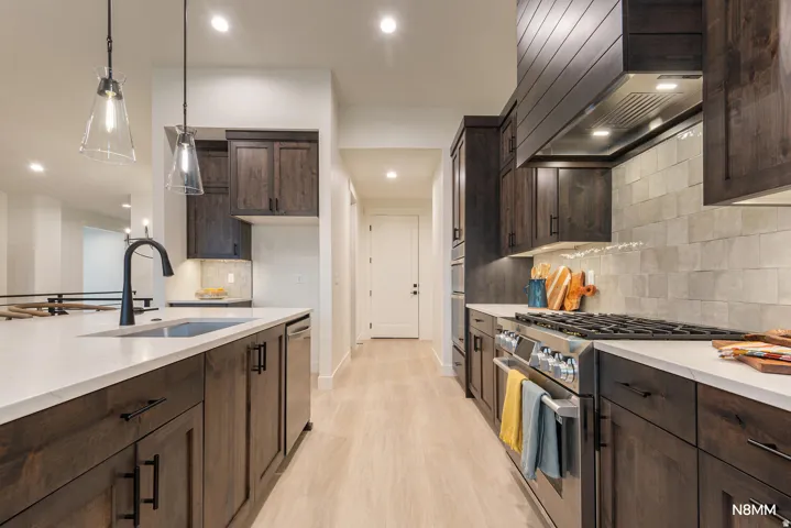 Kitchen with dark wood finish cabinets, stainless steel appliances, light stone countertops, light wood-style floors, and hanging light fixtures