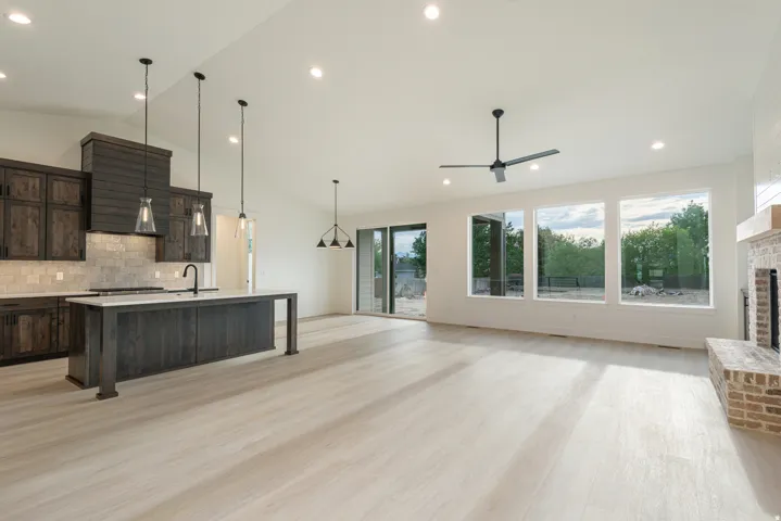 Kitchen featuring open floor plan, dark wood finish cabinetry, a kitchen island with sink, light wood-style flooring, and backsplash