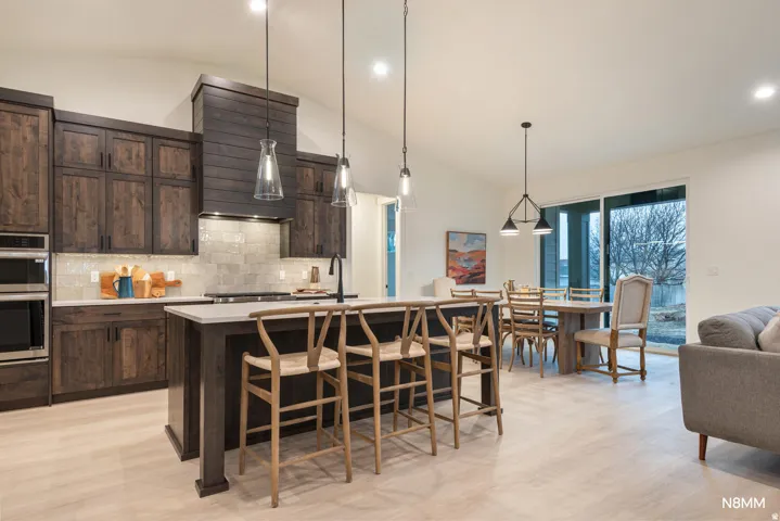 Kitchen with dark wood finish cabinetry, vaulted ceiling, a center island with sink, double oven, and light wood-style flooring