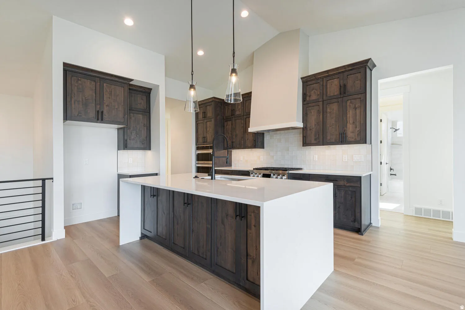 Kitchen with dark wood finish cabinetry, light stone countertops, an island with sink, pendant lighting, and tasteful backsplash