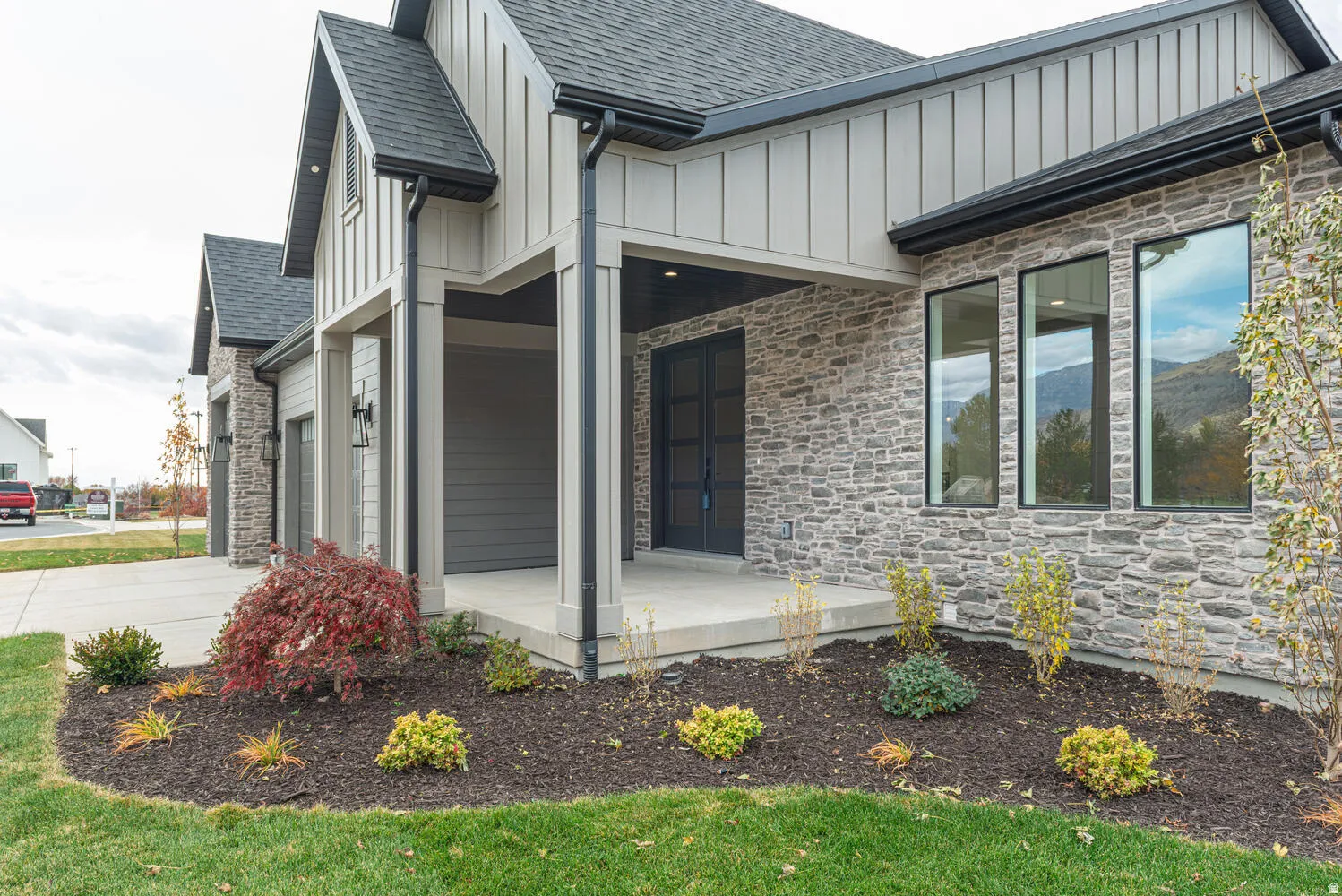 View of side of property with stone siding, board and batten siding, a shingled roof, a porch, and concrete driveway