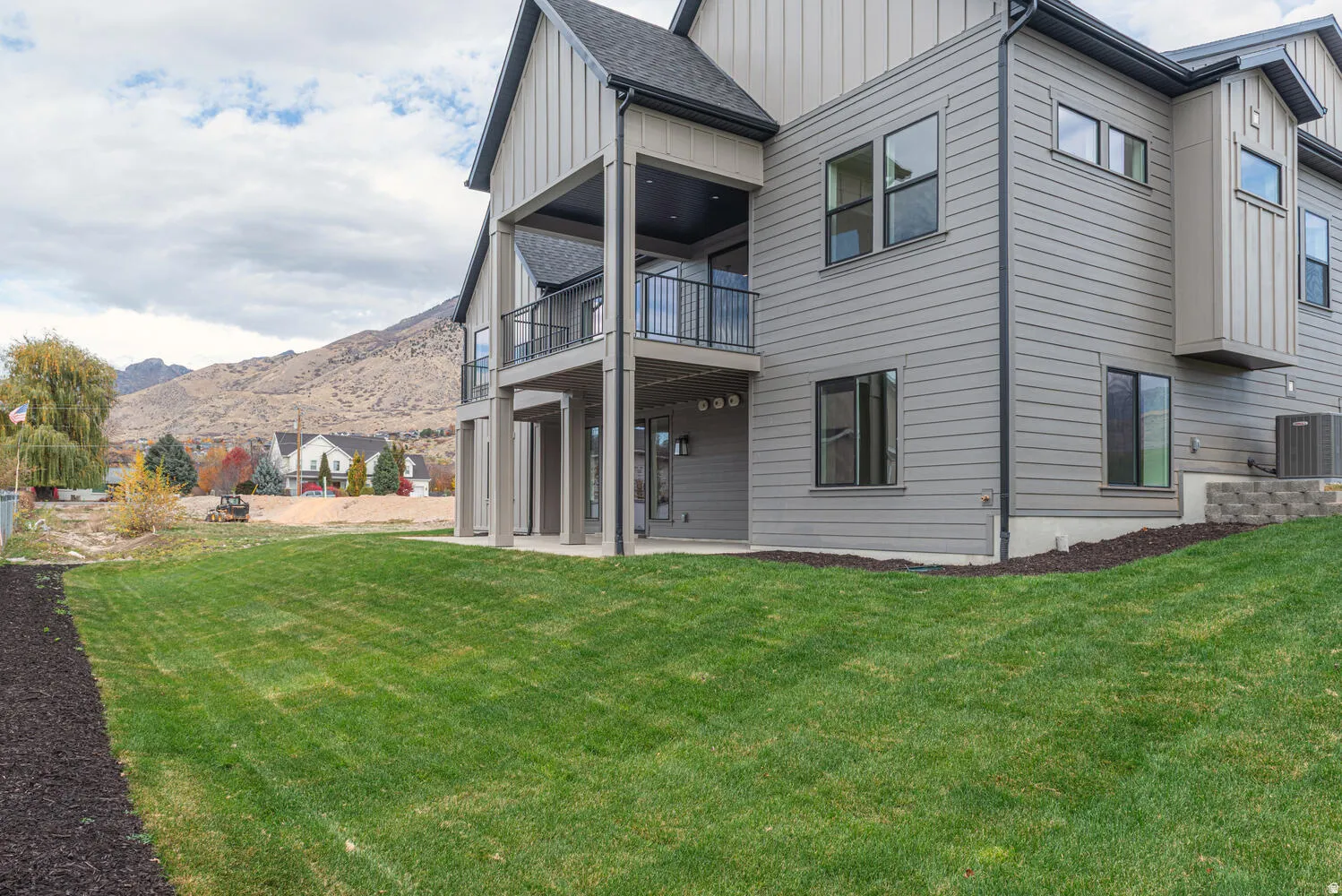 Rear view of house featuring board and batten siding, a patio, a balcony, a yard, and a mountain view