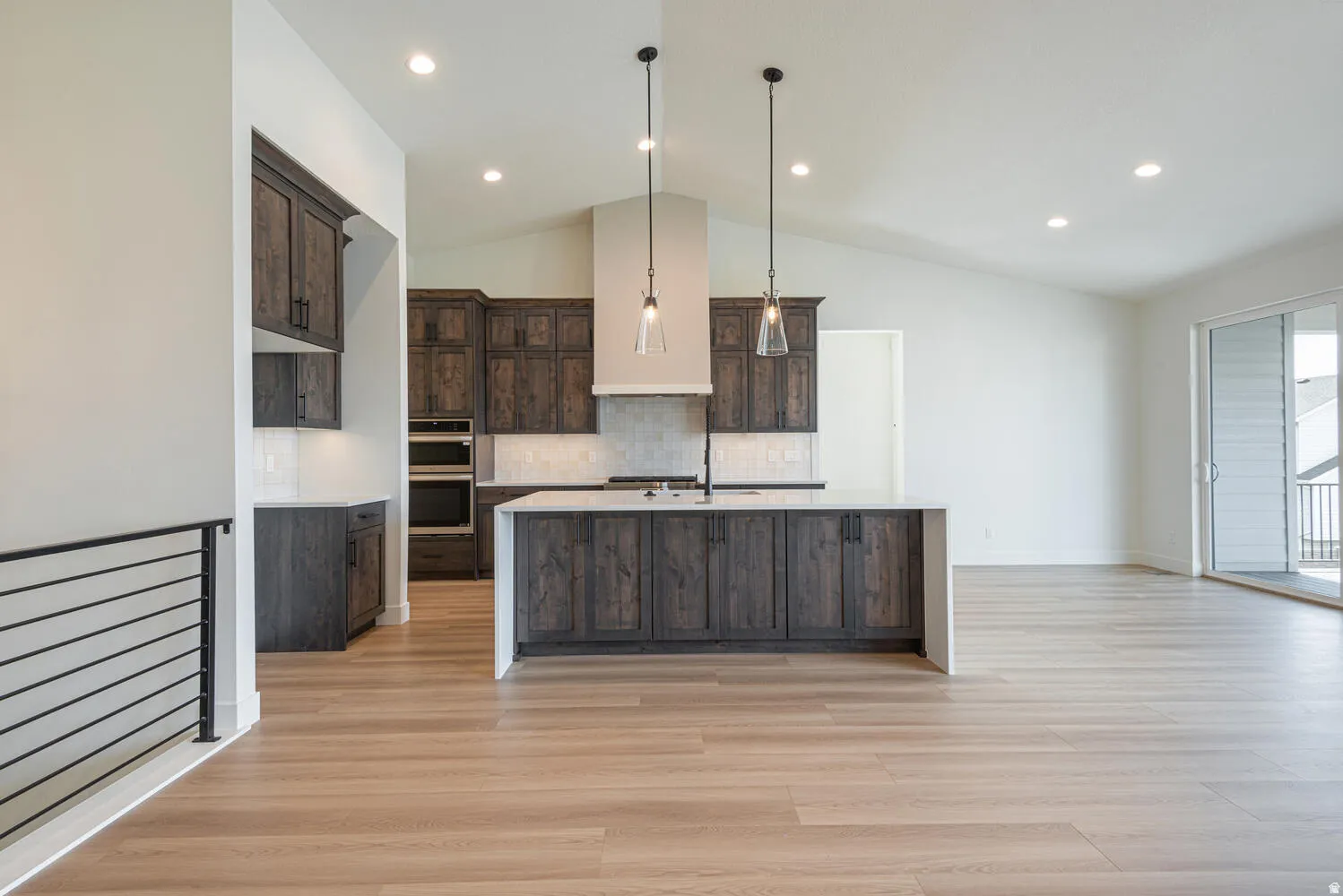 Kitchen featuring dark wood finish cabinets, a kitchen island with sink, decorative light fixtures, tasteful backsplash, and vaulted ceiling