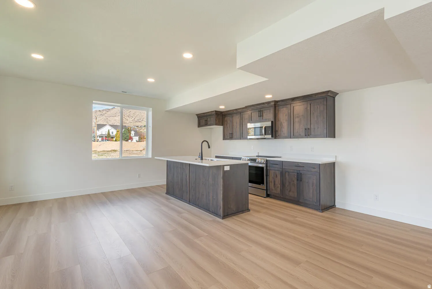 Kitchen with dark wood finish cabinetry, an island with sink, stainless steel appliances, light wood-style floors, and recessed lighting