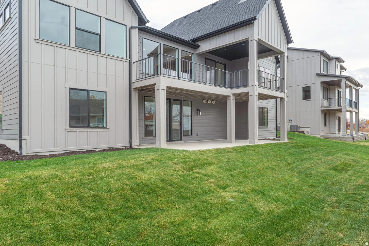 Rear view of house featuring board and batten siding, a patio area, a lawn, and a balcony