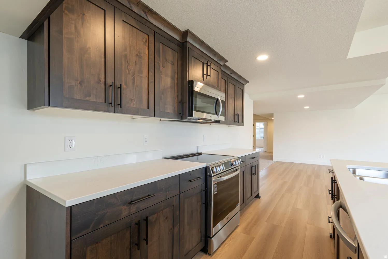 Kitchen featuring stainless steel appliances, dark wood finish cabinetry, light wood-style floors, recessed lighting, and a textured ceiling