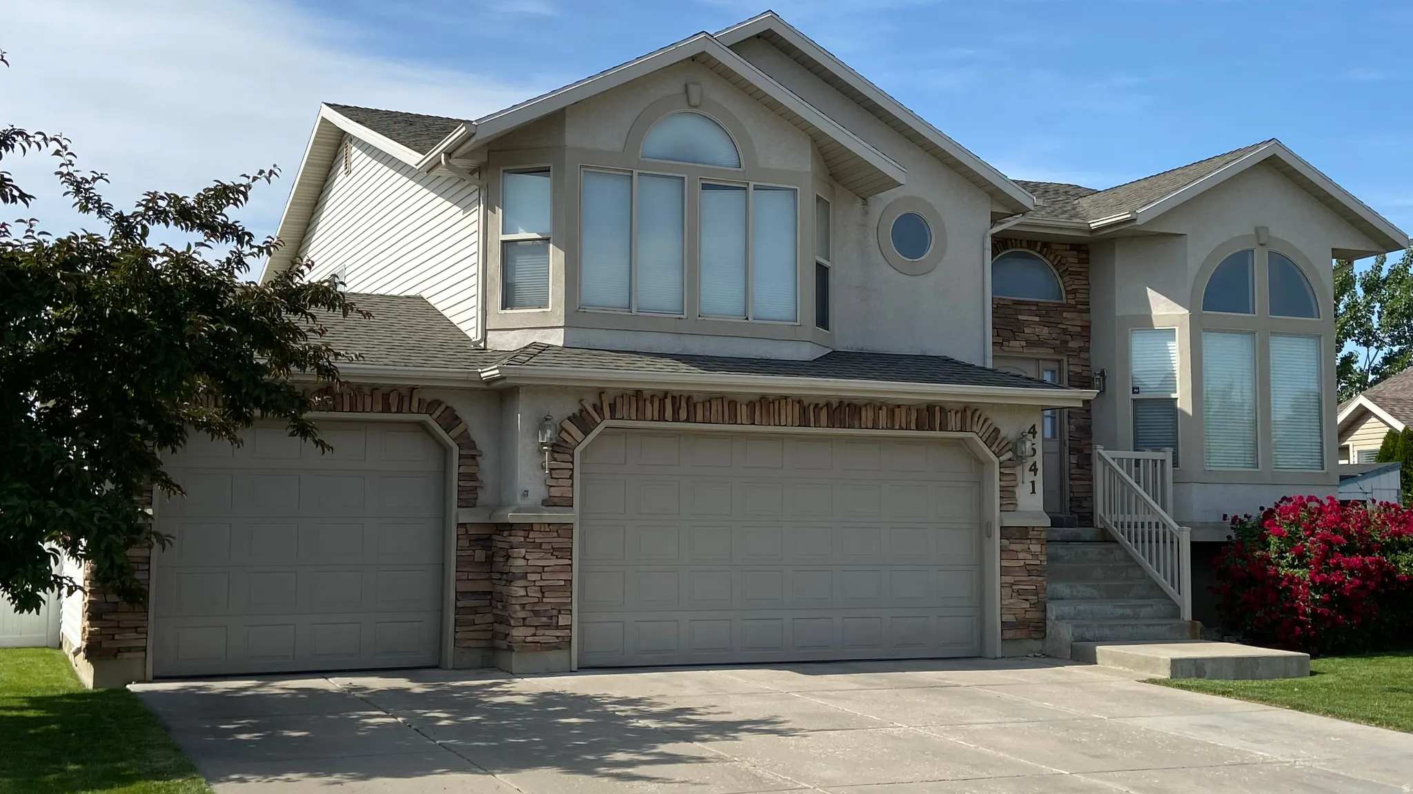 View of front of property with stone siding, roof with shingles, concrete driveway, a garage, and stucco siding