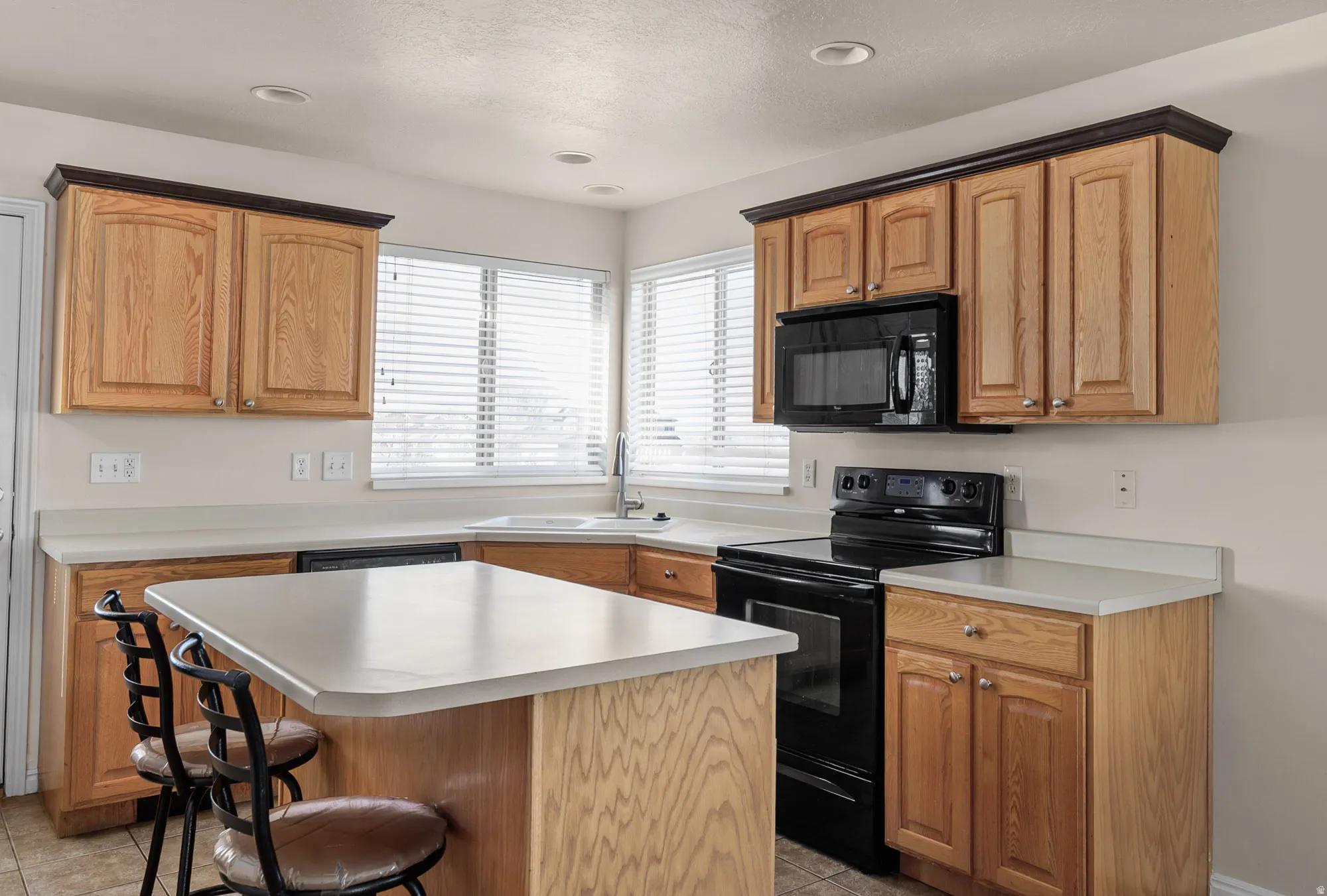 Kitchen with black appliances, a breakfast bar, light countertops, a center island, and wood finish cabinetry