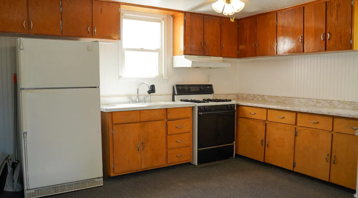 Kitchen featuring gas stove, freestanding refrigerator, light countertops, wood finish cabinets, and dark carpet