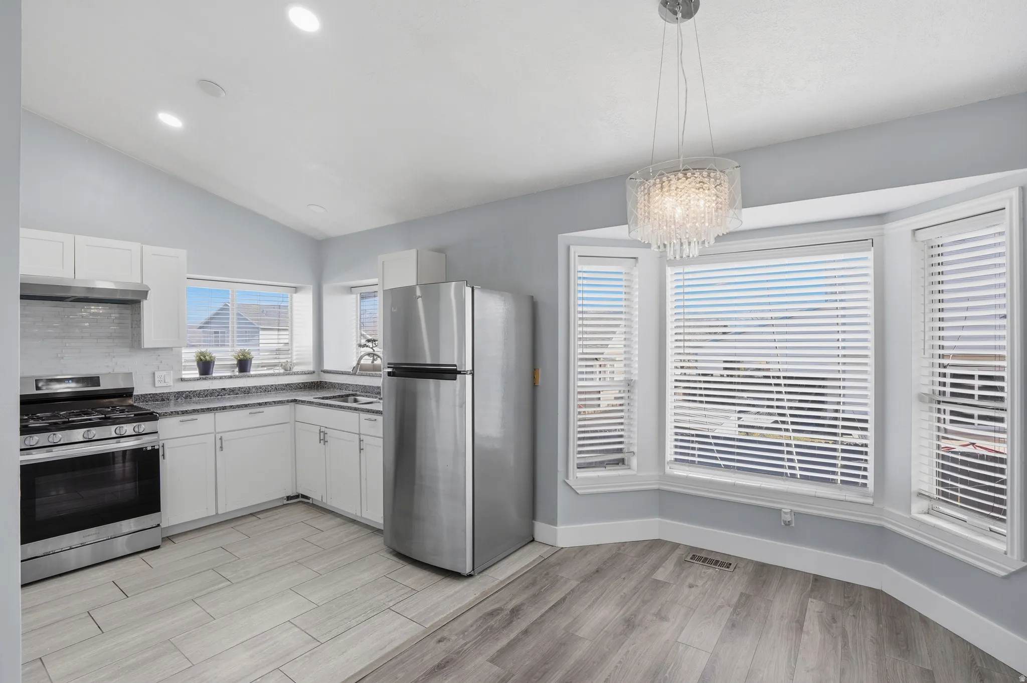 Kitchen with stainless steel appliances, wood tiled floors, white cabinetry, and vaulted ceiling