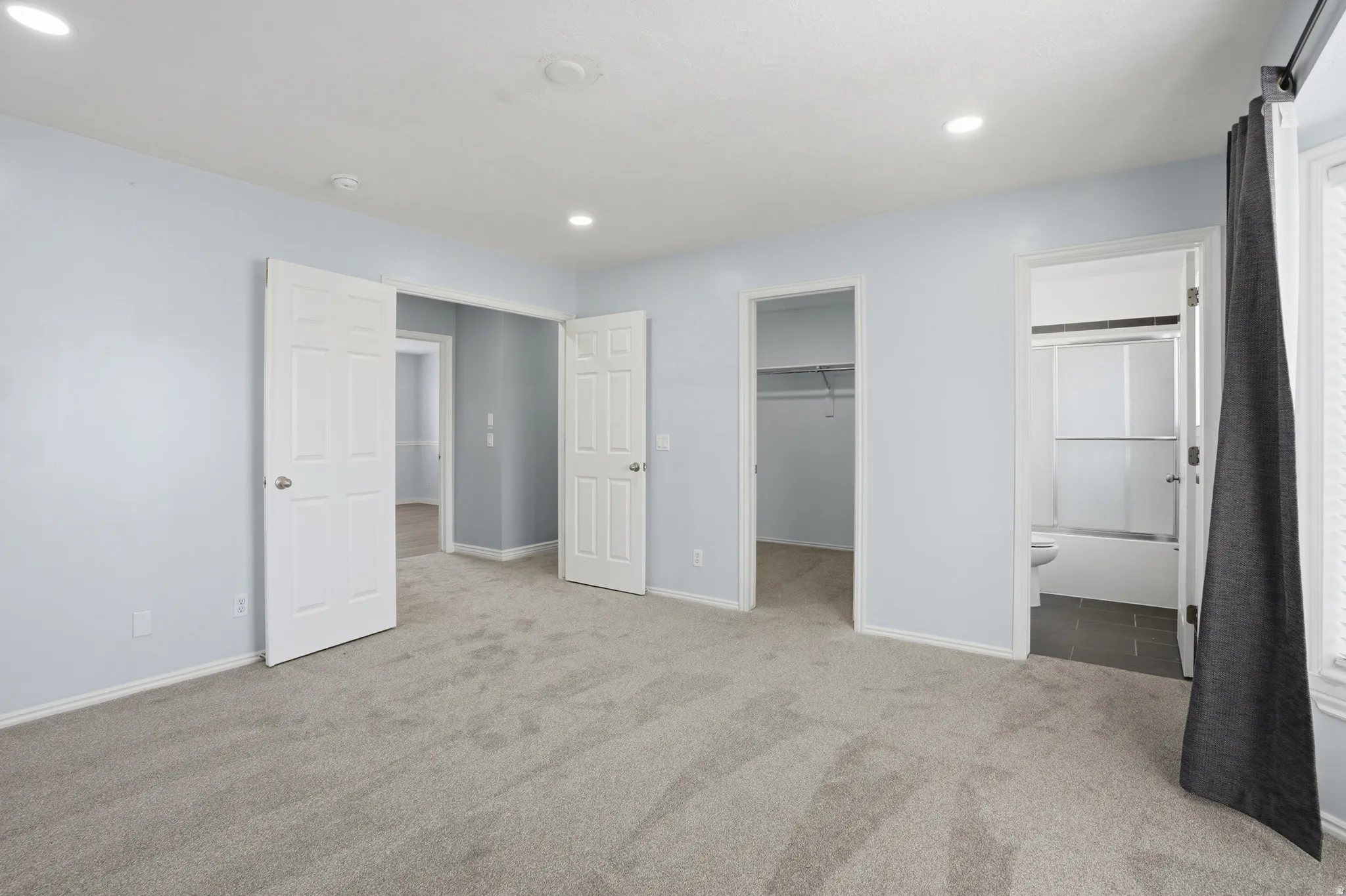 Unfurnished bedroom with a spacious closet, ensuite bath, light carpet, and recessed lighting