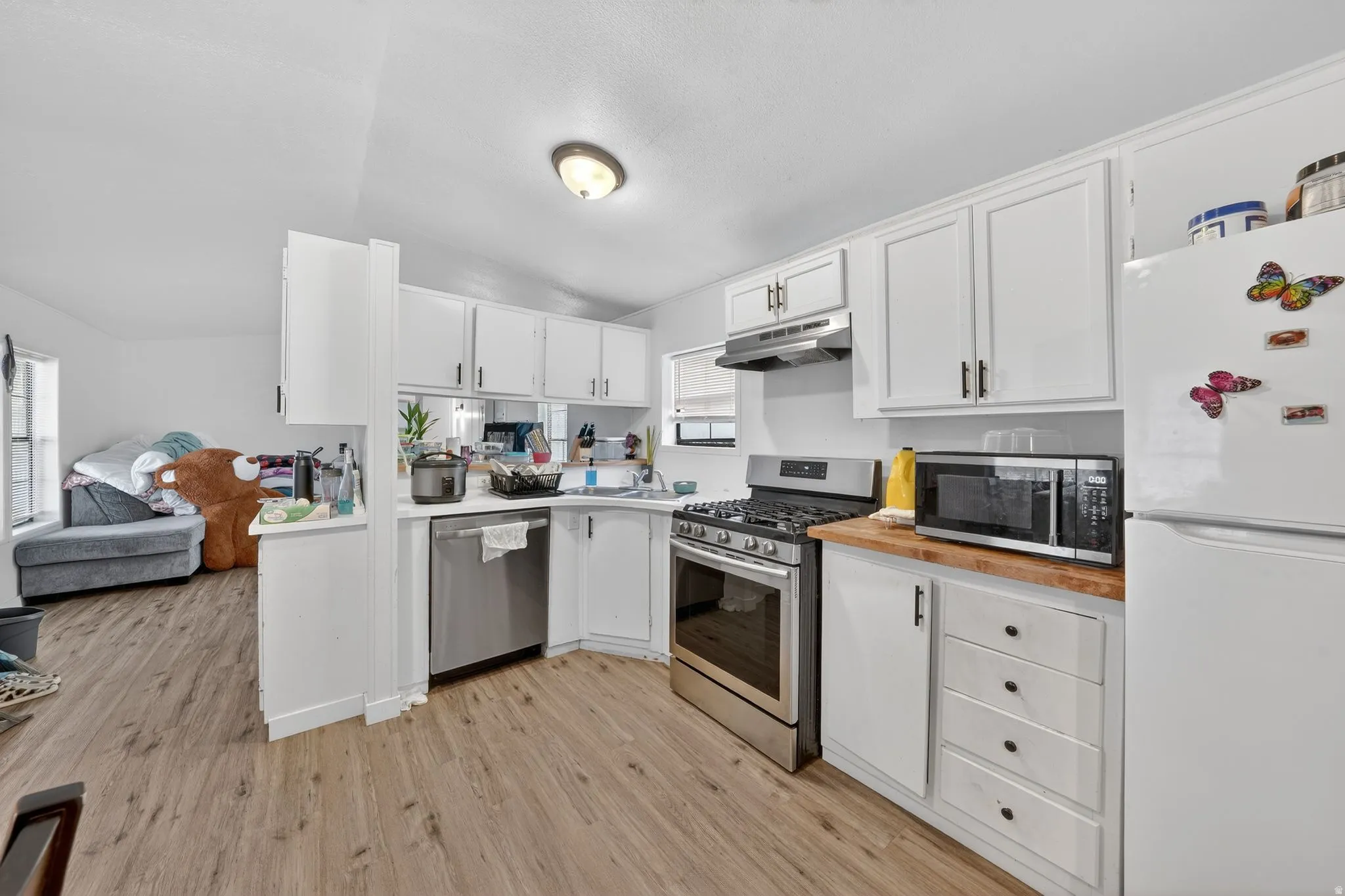 Kitchen featuring stainless steel appliances, white cabinetry, wood counters, light wood-style floors, and lofted ceiling