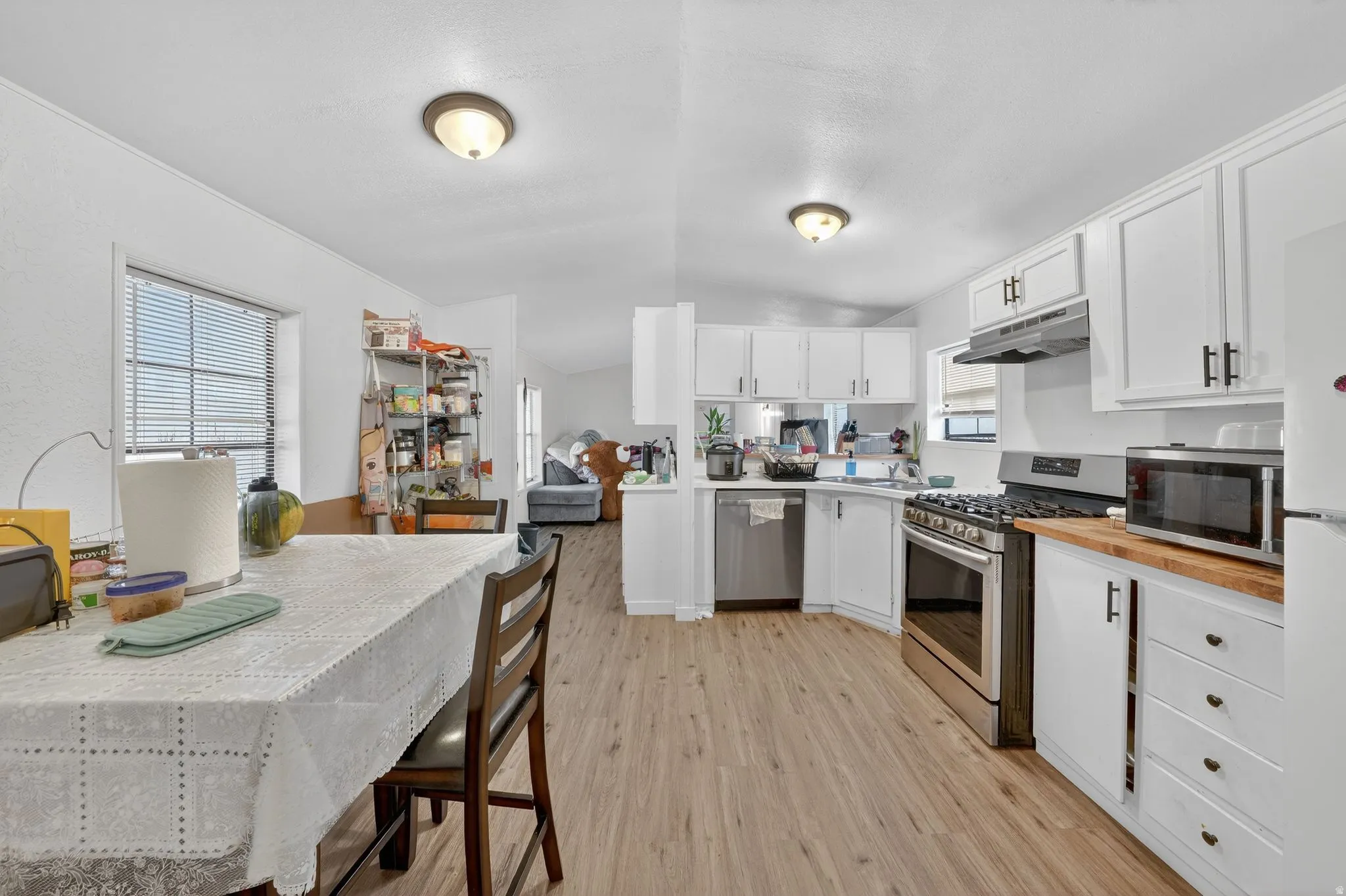 Kitchen with stainless steel appliances, butcher block counters, white cabinetry, vaulted ceiling, and light wood-type flooring