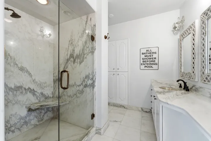 Full bathroom featuring vanity, a marble finish shower, and light marble finish flooring