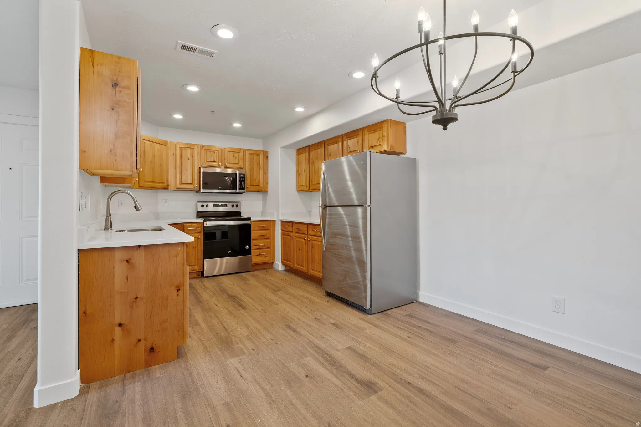 Kitchen with stainless steel appliances, a chandelier, and light wood-type flooring