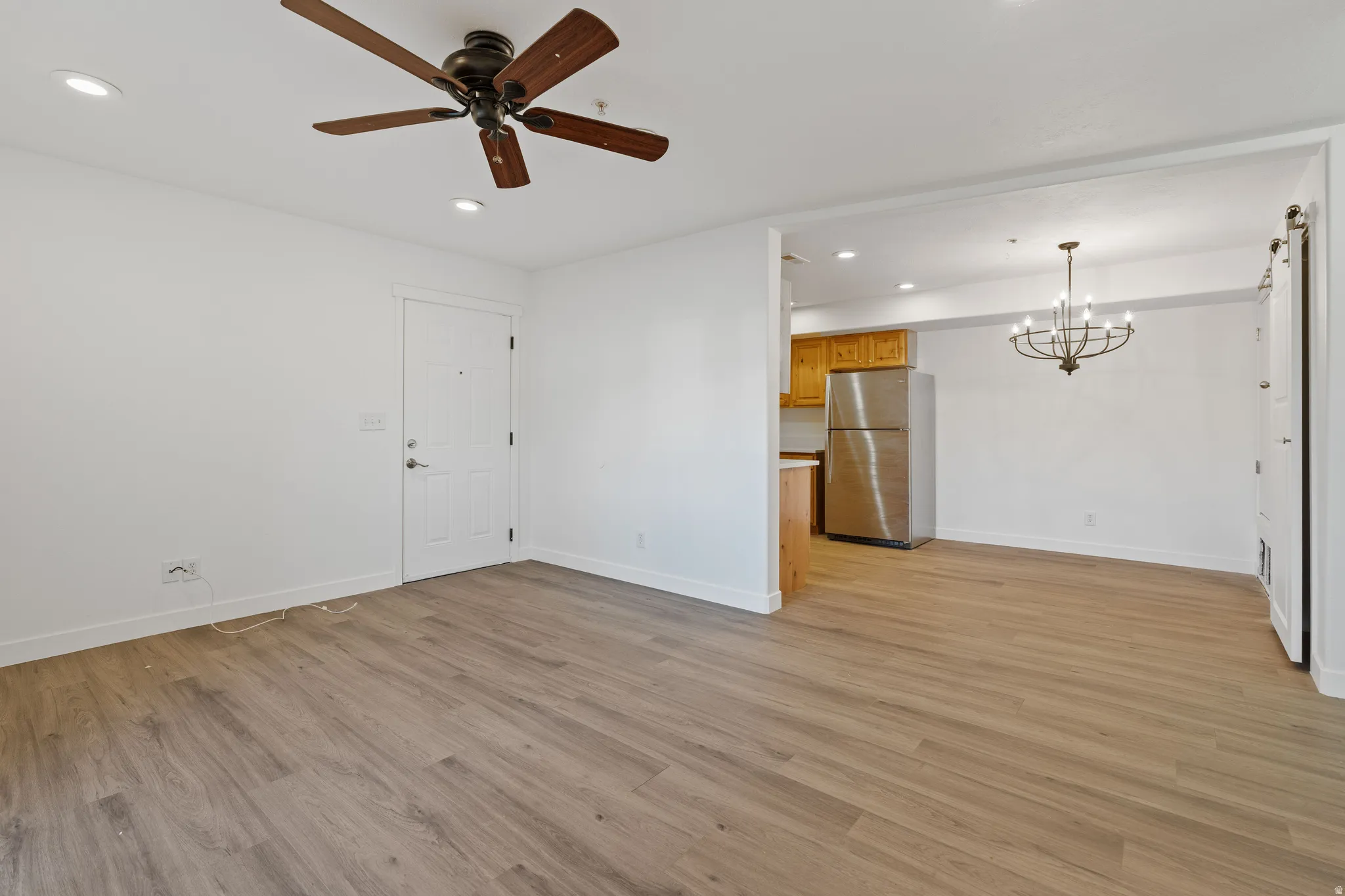 Unfurnished living room featuring a chandelier, ceiling fan, and light wood finished floors