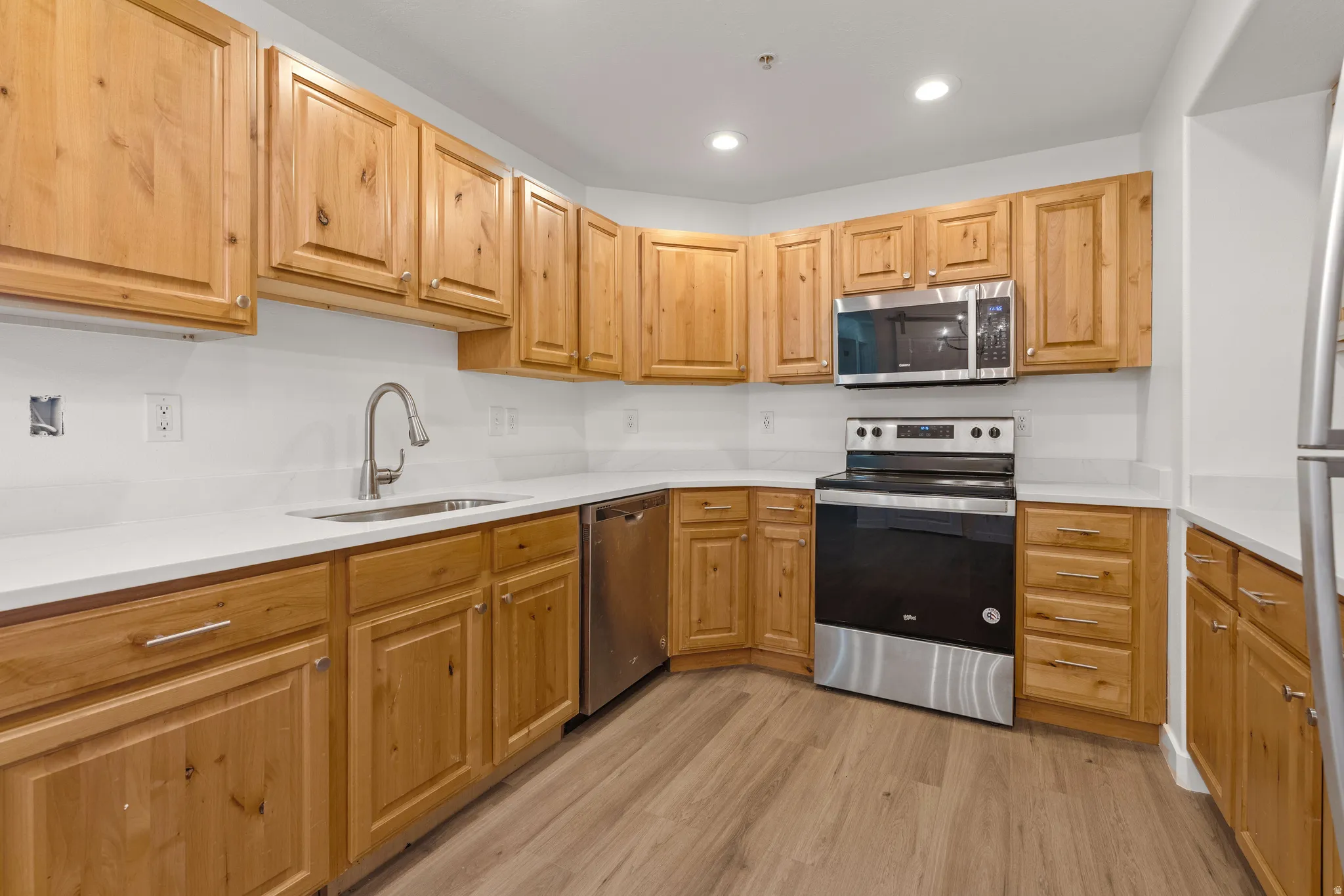 Kitchen with stainless steel appliances, light wood-type flooring, recessed lighting, and light stone countertops