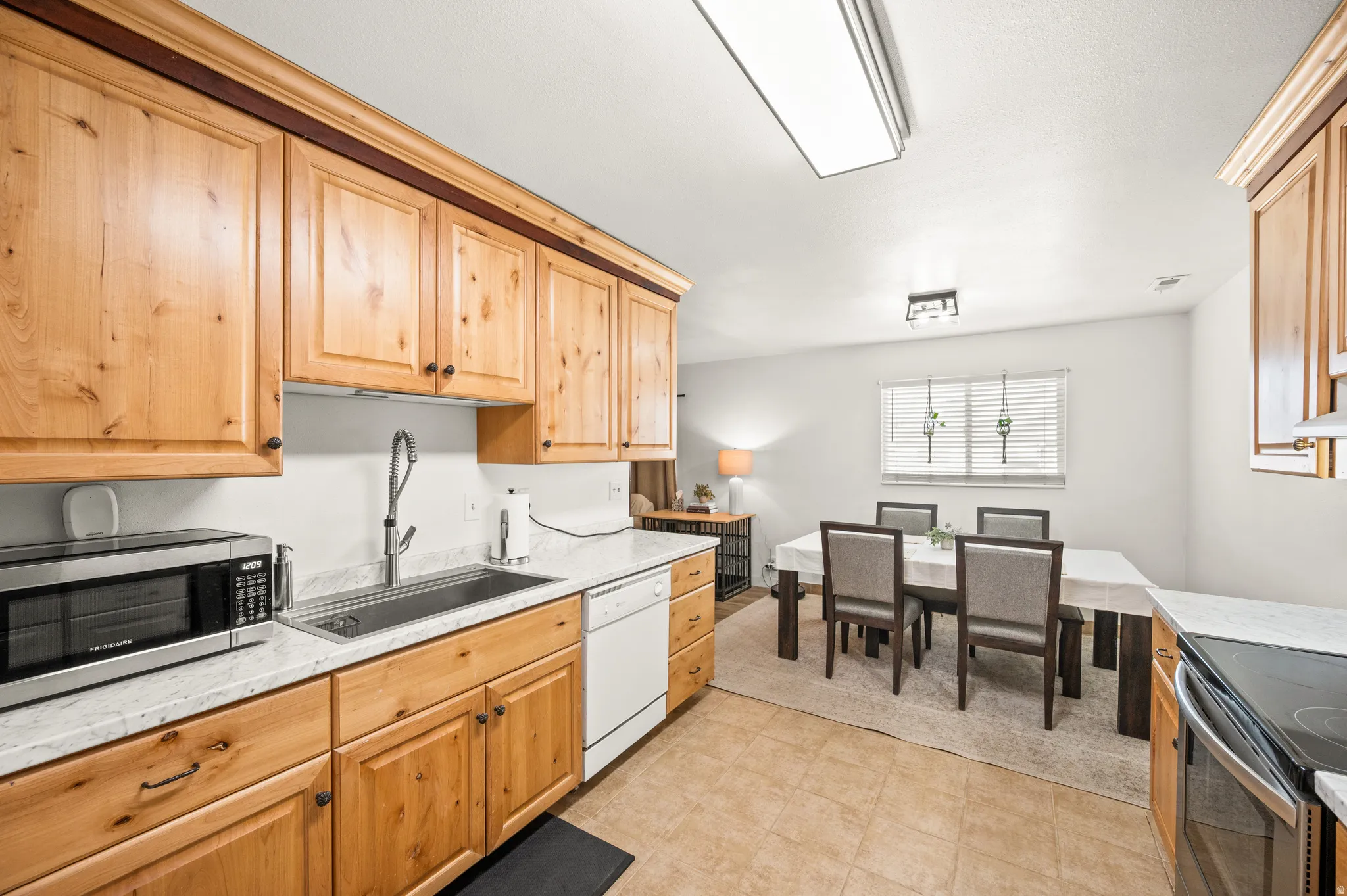Kitchen featuring stainless steel appliances, light stone countertops, light flooring, and light wood finish cabinets