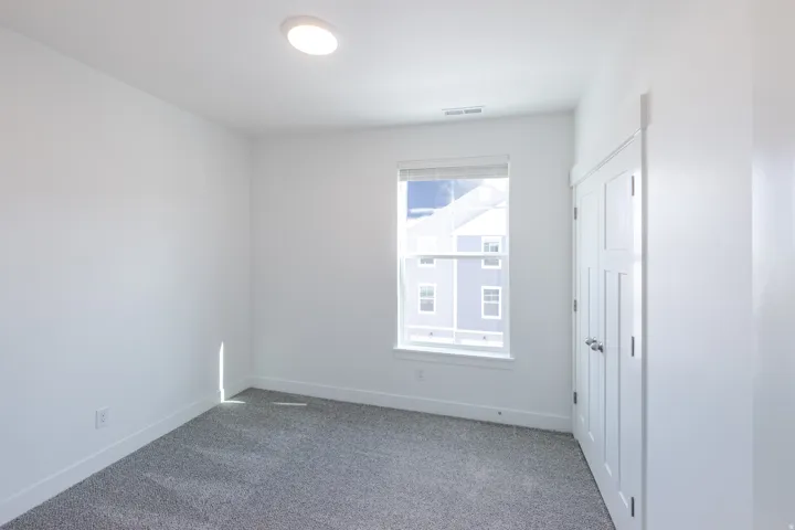 Recessed lighting, white walls, gray carpet, single window with roller shade, and a white paneled door