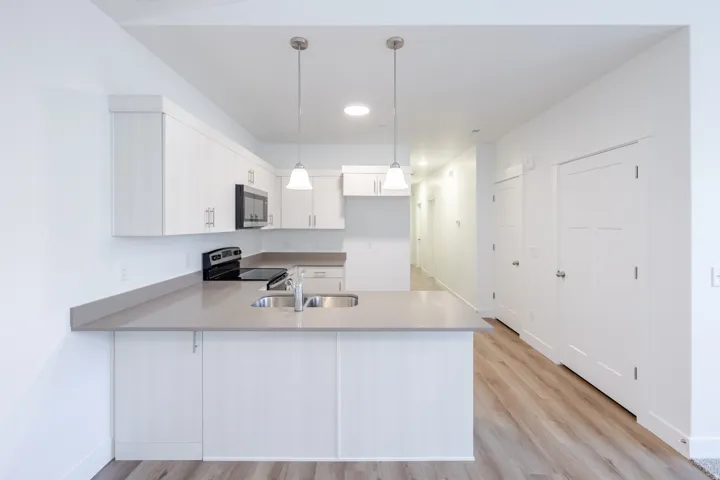 Kitchen featuring light wood-finish flooring, white cabinetry with silver-tone hardware, a stainless steel sink, and light gray countertops