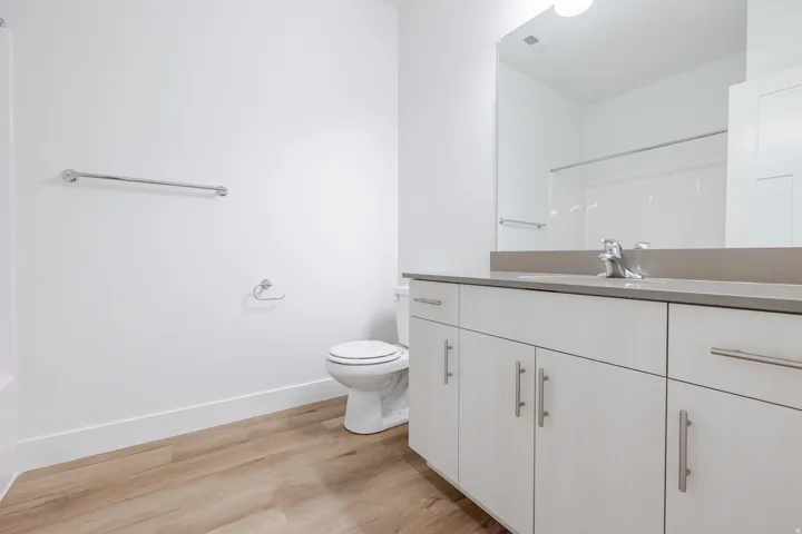 Spa-inspired bathroom featuring a white vanity with multiple storage cabinets, wood-finish flooring, and a large framed mirror above a quartz countertop