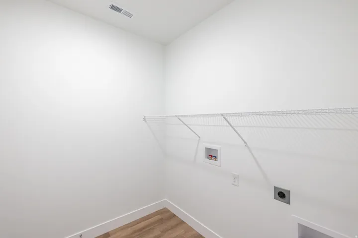 Utility room with wood-finish flooring, white walls, and a white wire shelf