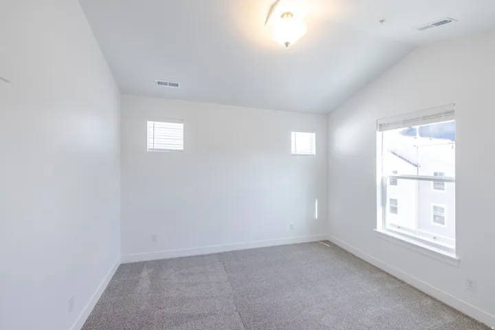 Vaulted ceiling, recessed lighting, neutral carpet, white walls, and multiple windows