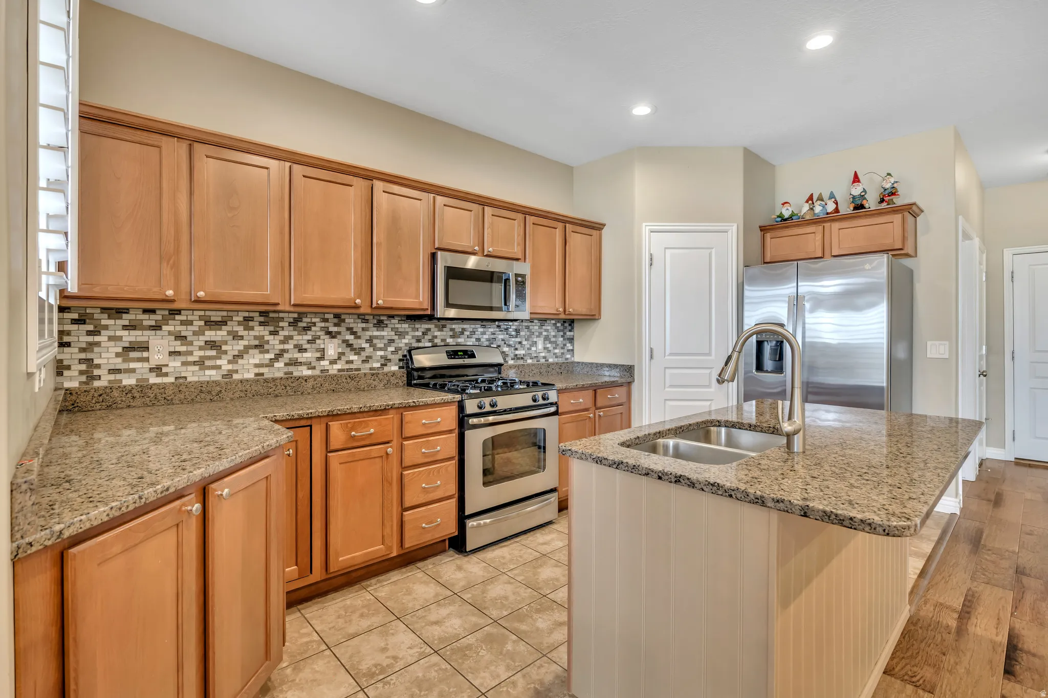 Kitchen with stainless steel appliances, light stone counters, a center island with sink, wood finish cabinetry, and tasteful backsplash
