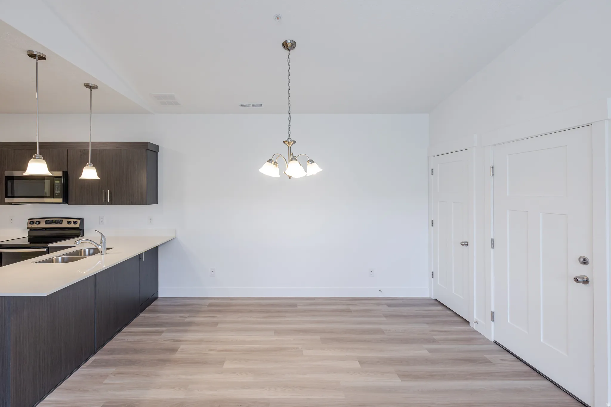 Open-concept living space featuring wood-finish flooring, dark wood-finish cabinetry, stainless steel appliances, and white countertops